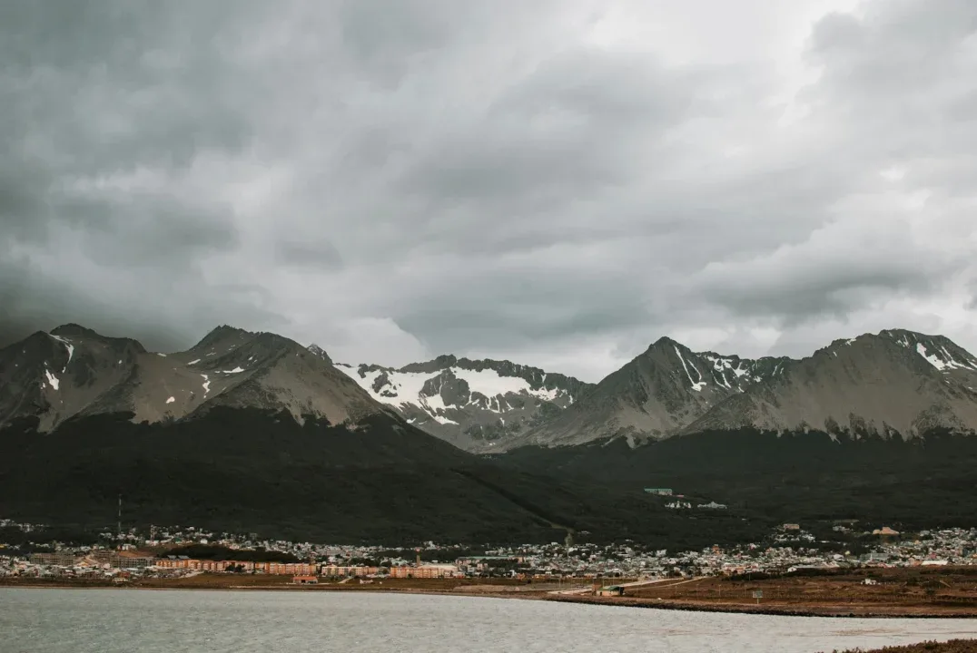 a lake surrounded by mountains under a cloudy sky