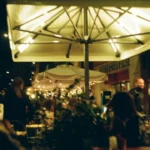 a group of people sitting at tables under an umbrella